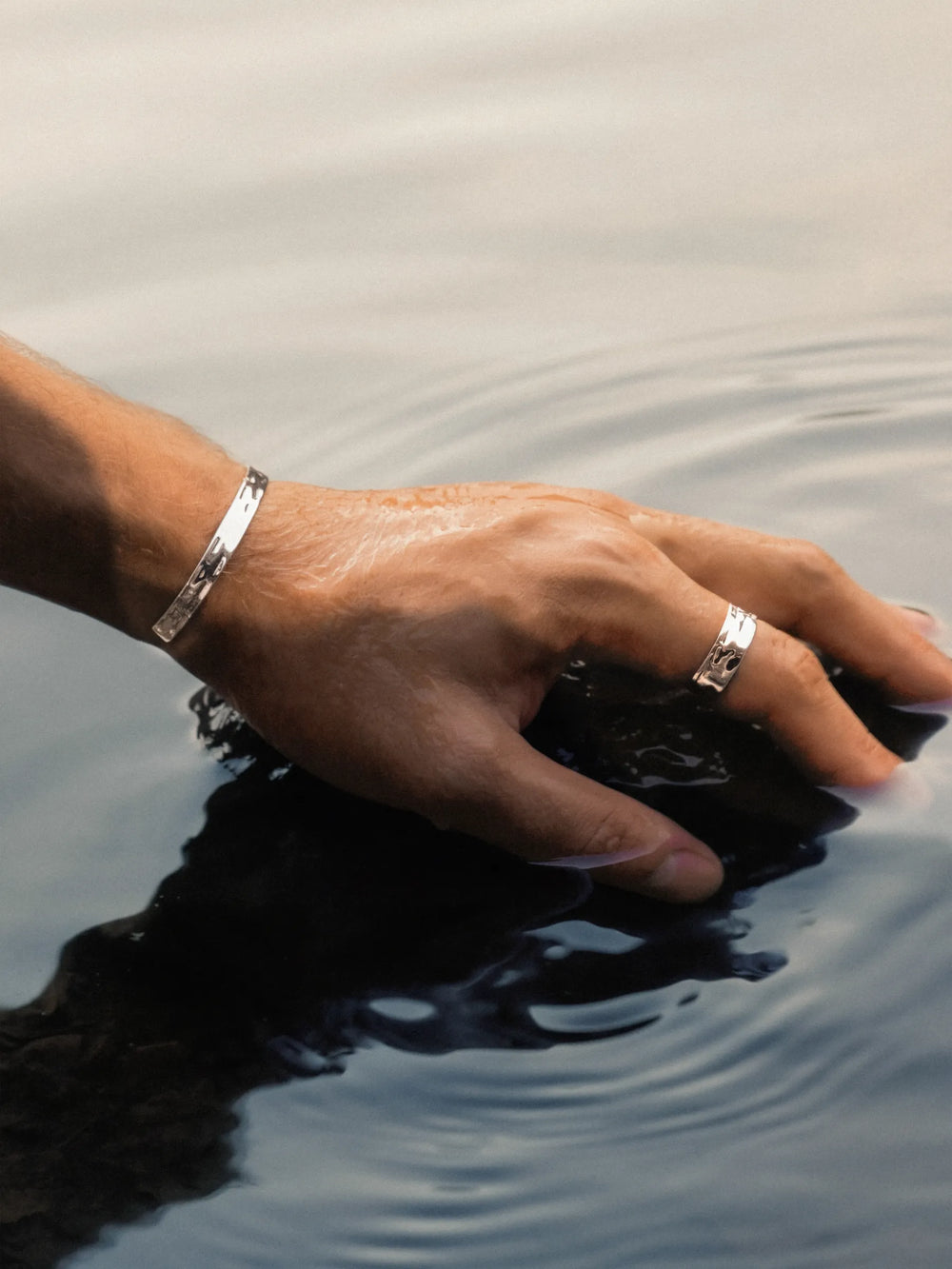 Hand with a ring and bracelet touching water