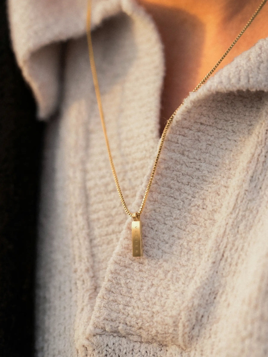 Gold necklace with a pendant on a person wearing a light-colored sweater.