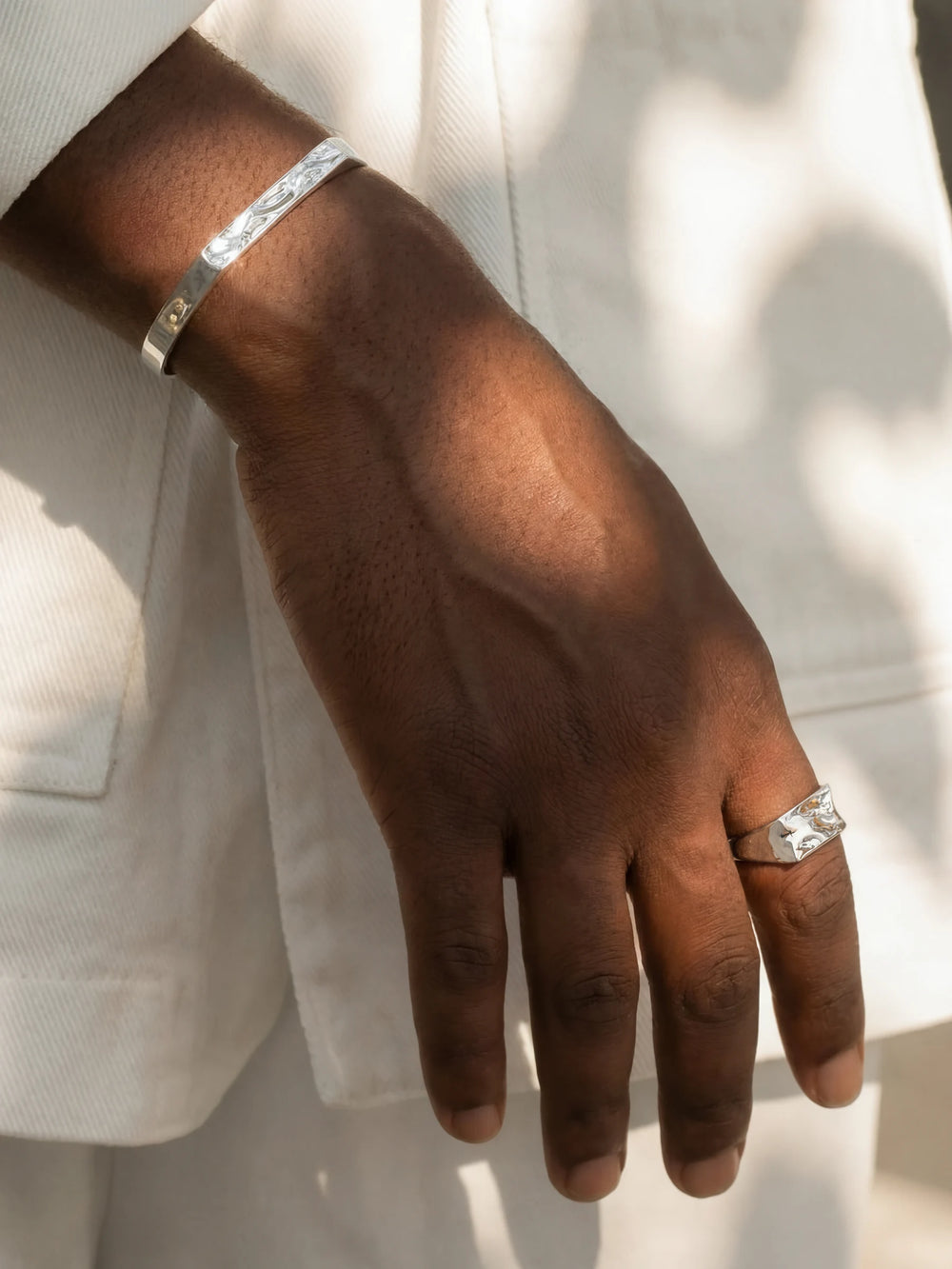 Hand wearing a silver bracelet and ring on a light background