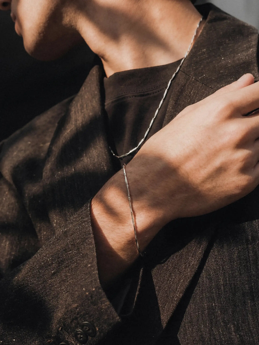 Person wearing a silver necklace and bracelet with a dark coat and shirt