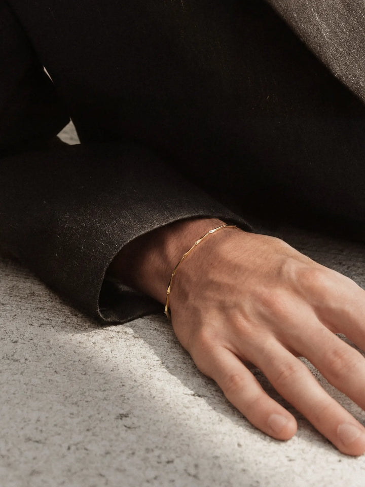 Hand wearing a gold bracelet on a textured surface