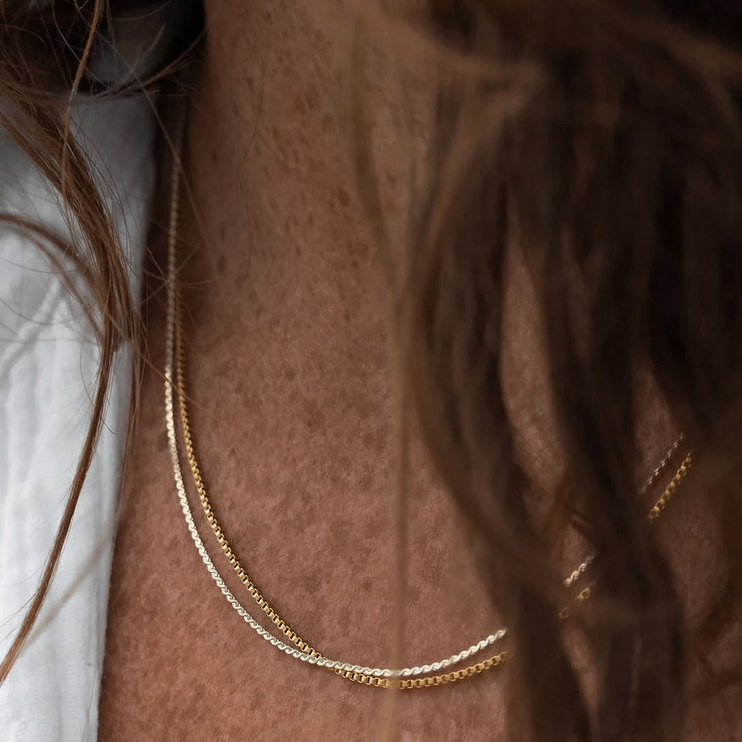 Close-up of a gold and a silver chain necklace on a person's neck.