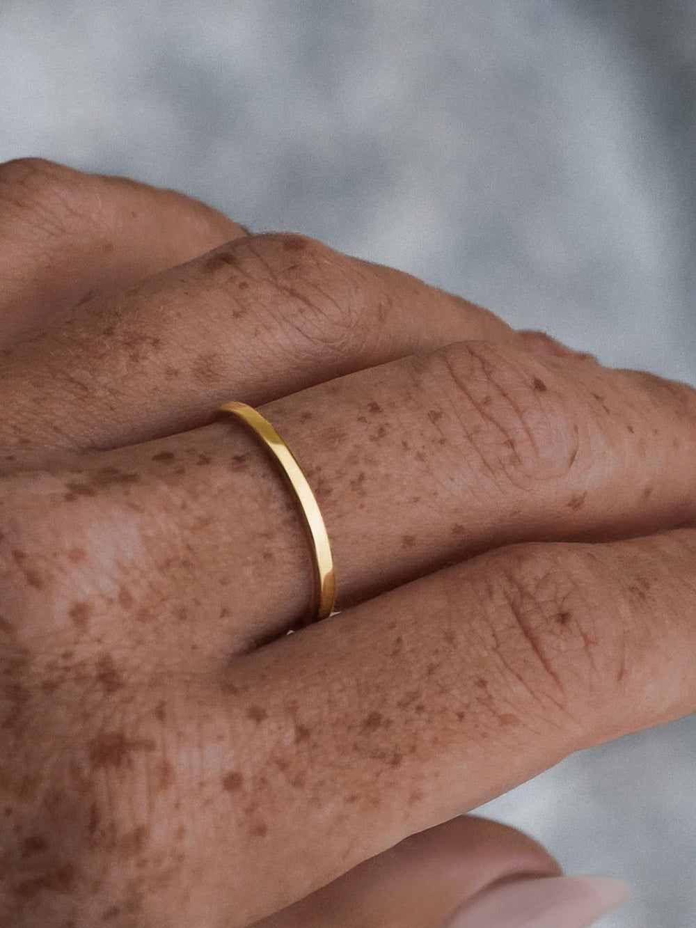 Gold vacier linear ring on a person's finger with a blurred background