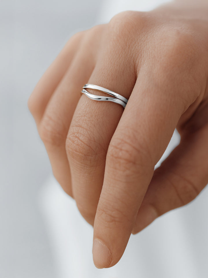 Stacked Silver vacier linear and fluid rings on a finger against a light background