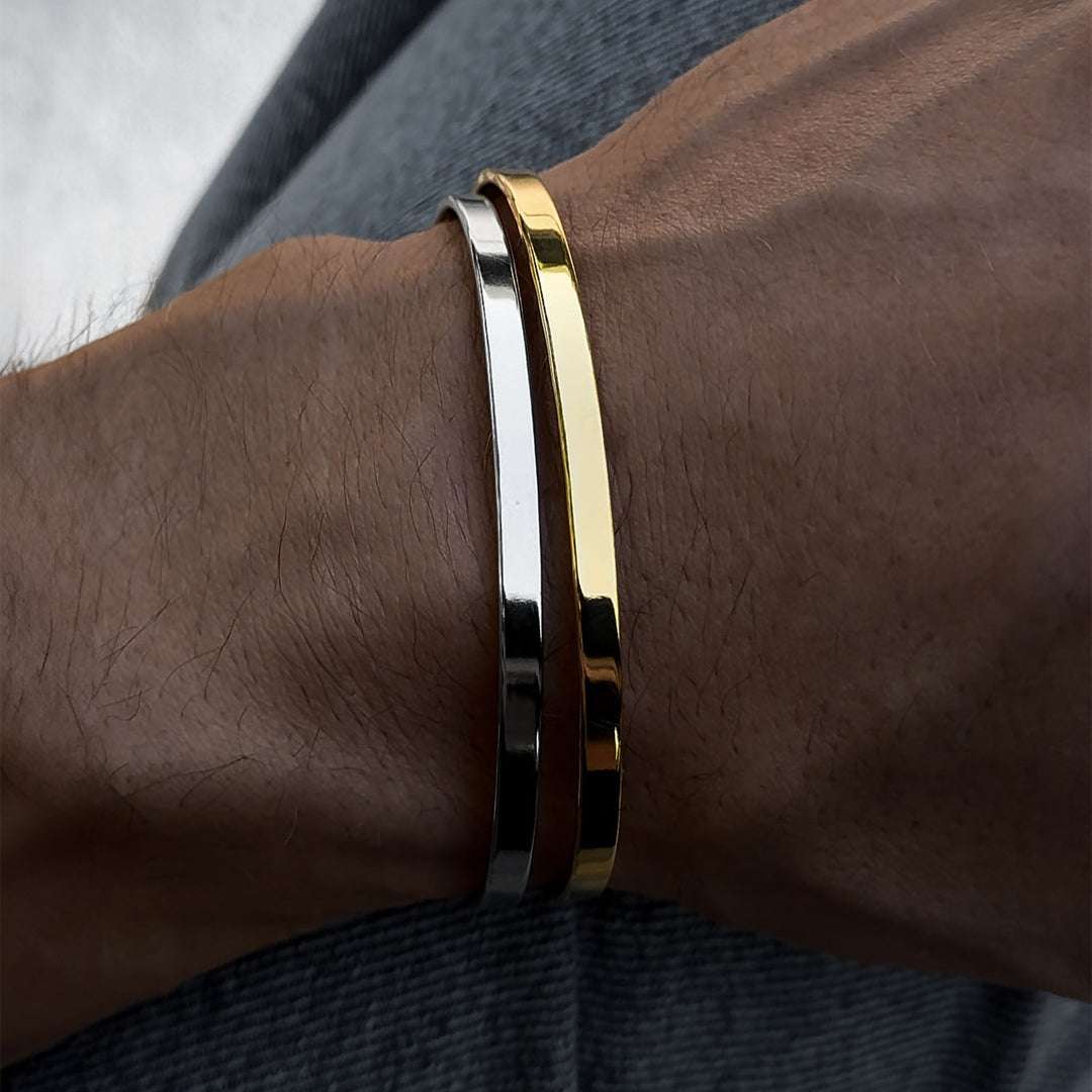 A gold and a silver cuff on a wrist against a dark fabric background