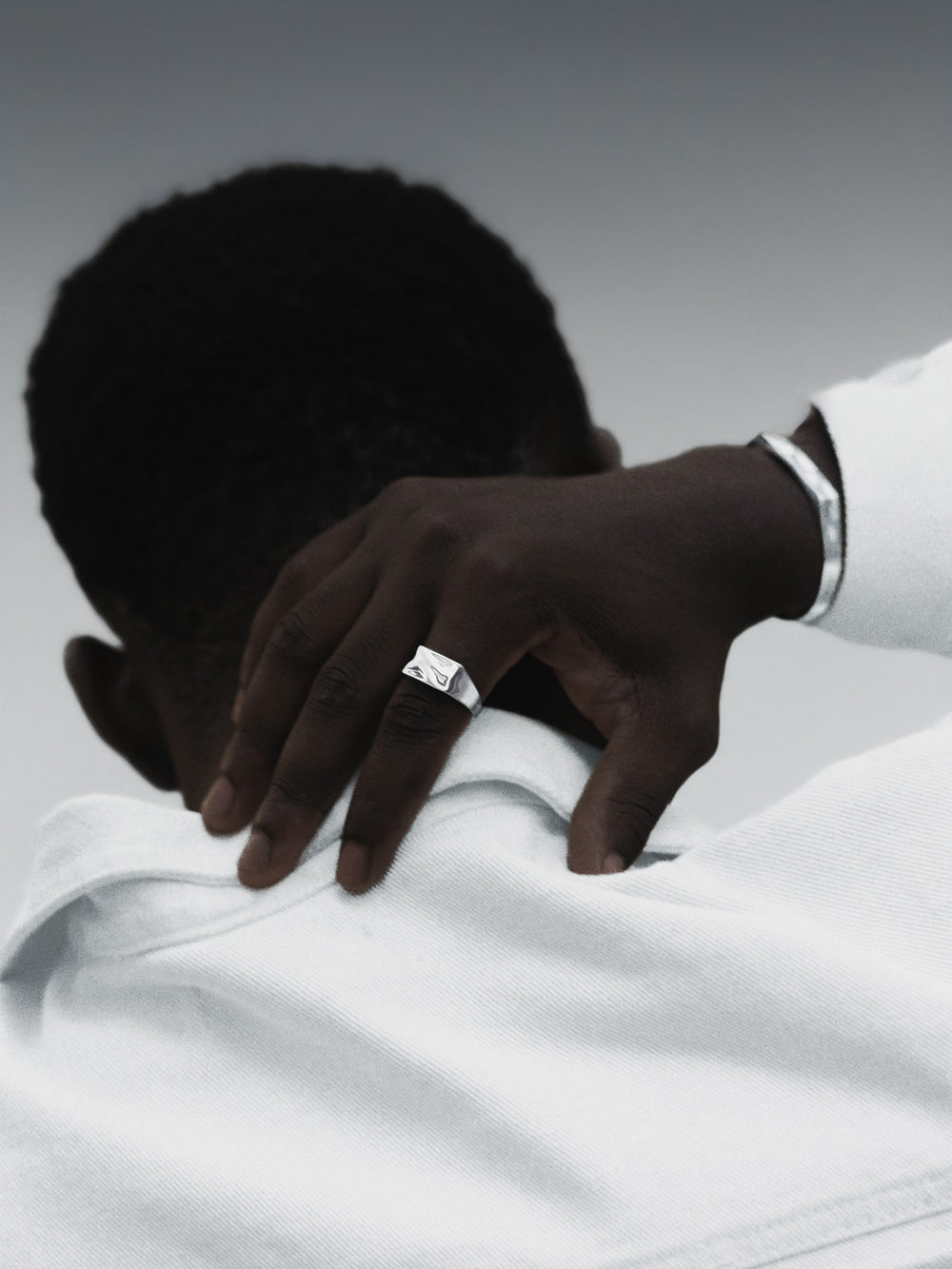 Hand with a ring on a white shirt against a gray background
