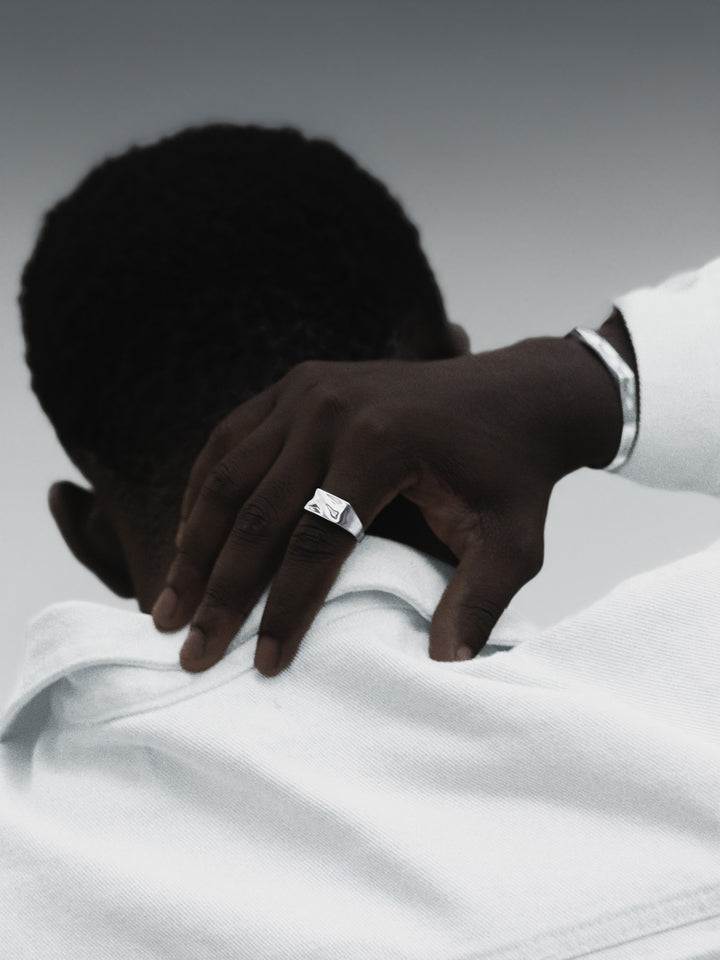 Hand with a ring on a white shirt against a gray background