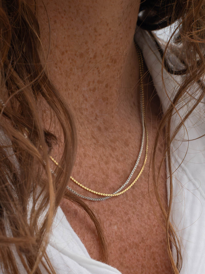 Close-up of a person wearing a gold and a silver necklace.