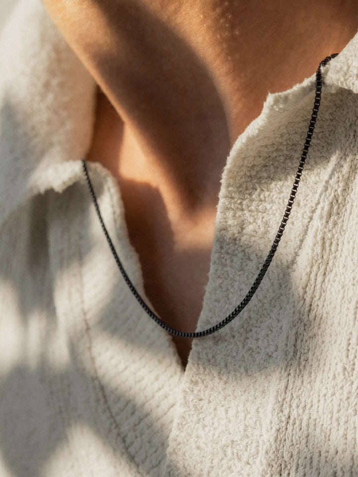 Person wearing a light colored sweater with a black necklace.
