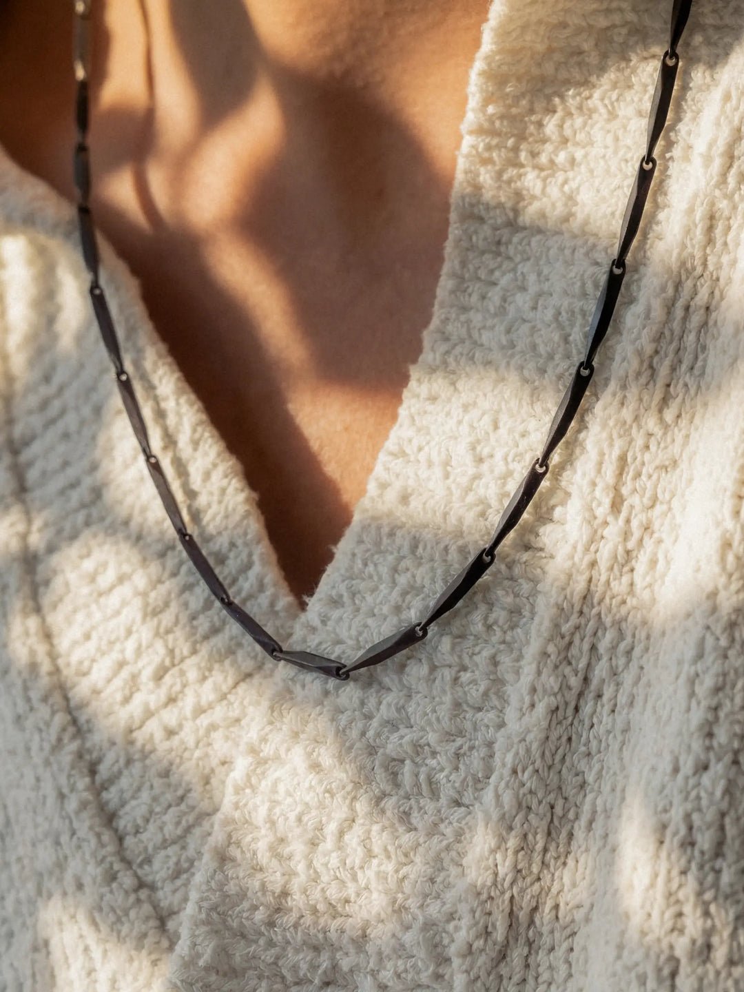 Close-up of a person wearing a black necklace with a light-colored shirt