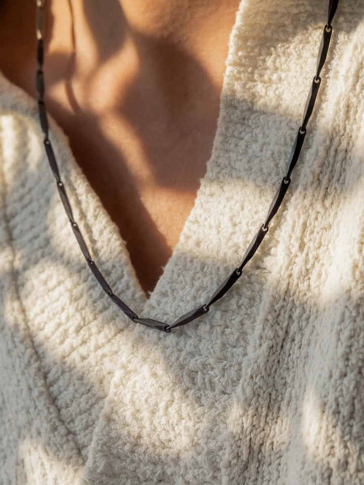 Close-up of a person wearing a black necklace with a light-colored shirt