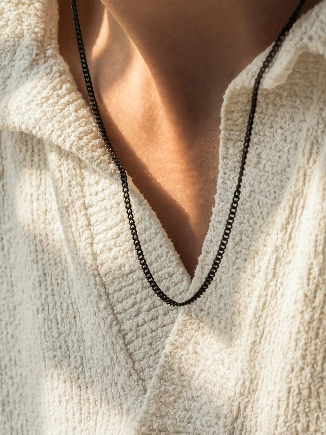 Close-up of a person wearing a black necklace with a light-colored shirt