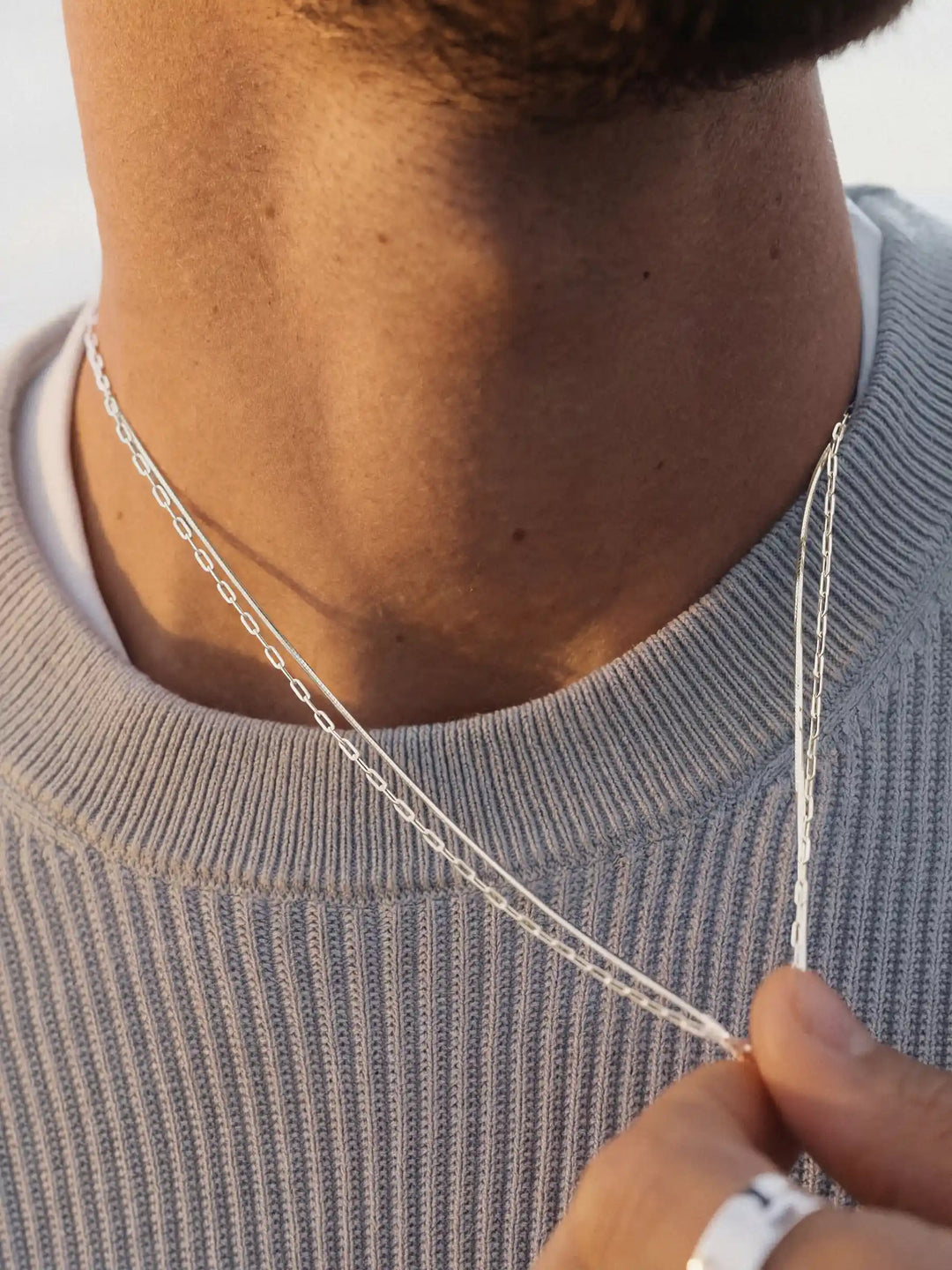 Close-up of two silver necklaces on a person wearing a light gray sweater.