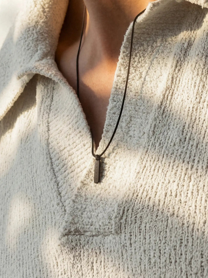 A close-up of a person wearing a black chain necklace with a rectangular pendant and a light-colored shirt