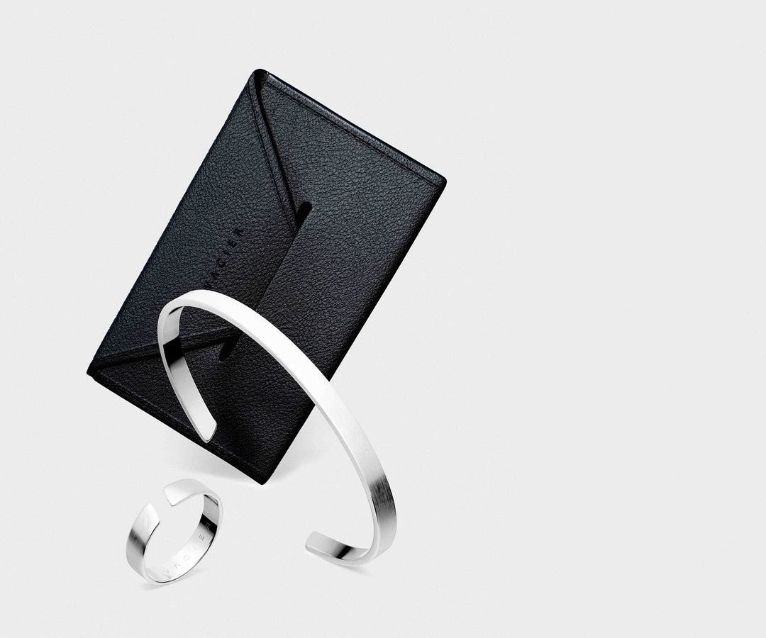 Black leather cardholder with a silver ring and cuff on a light gray background