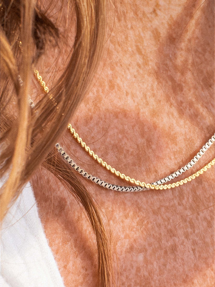 Two gold and silver necklaces on a person's neck