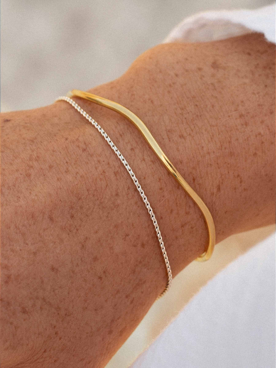 Gold cuff and a gold bracelet on a person's wrist against a blurred light background