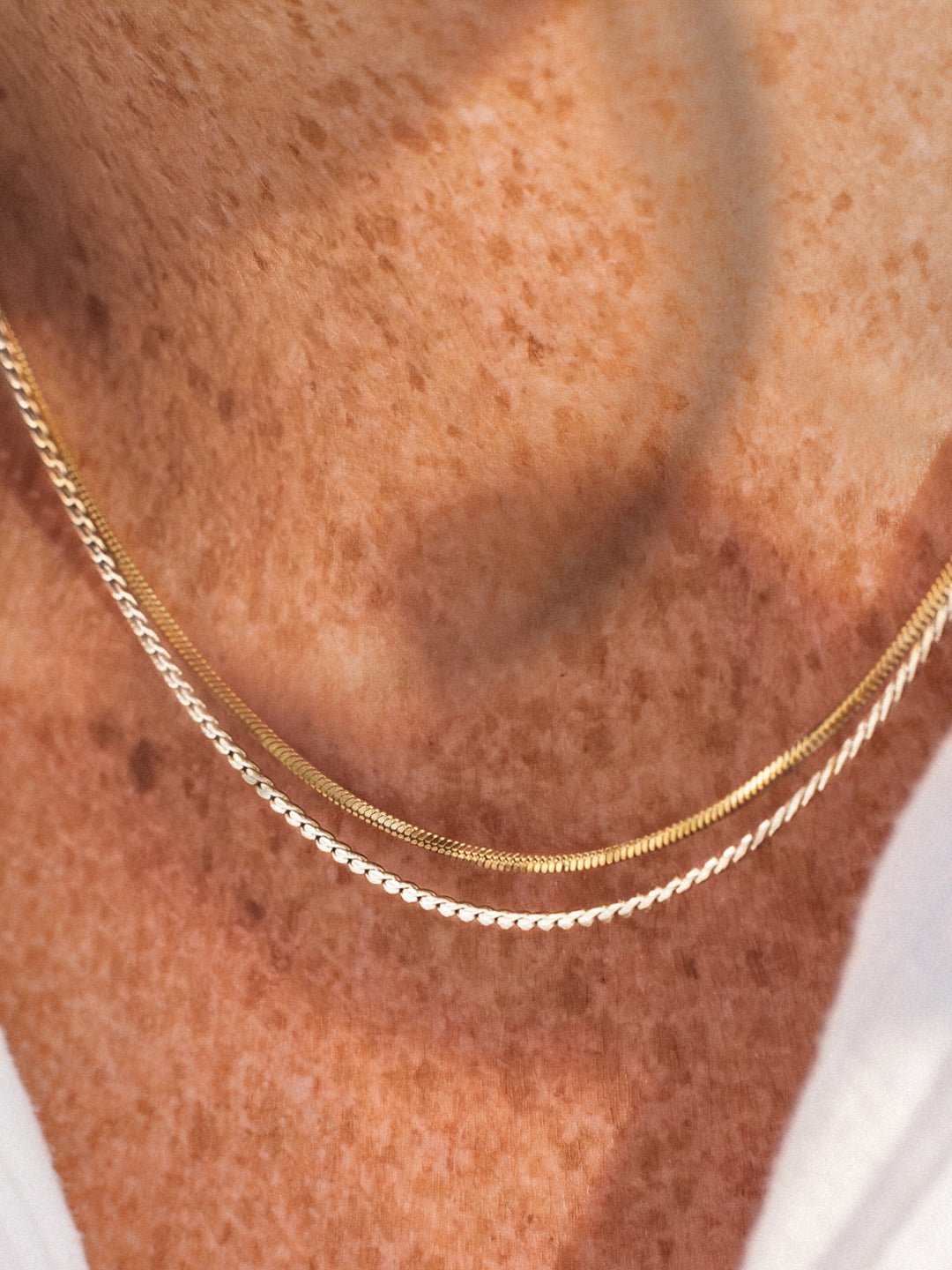 Gold and silver chain necklaces on a person's neck