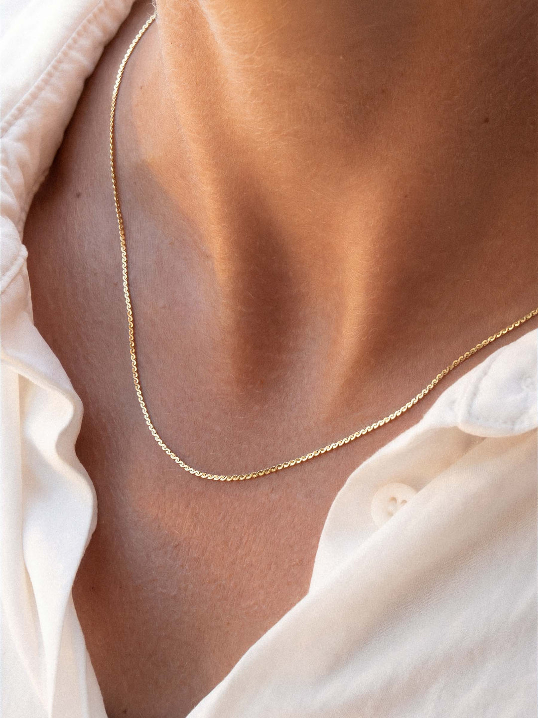 Gold necklace on a person wearing a light-colored shirt