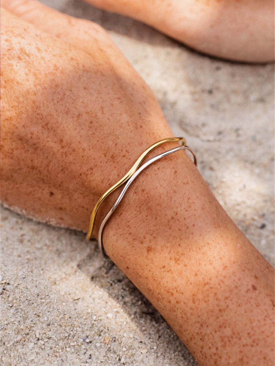 Gold and silver bracelets on a person's wrist against a neutral background