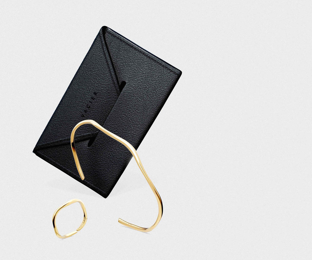 Black leather cardholder with gold cuff and ring on a light gray background