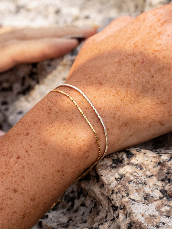 Gold and silver bracelets on a wrist with a natural background