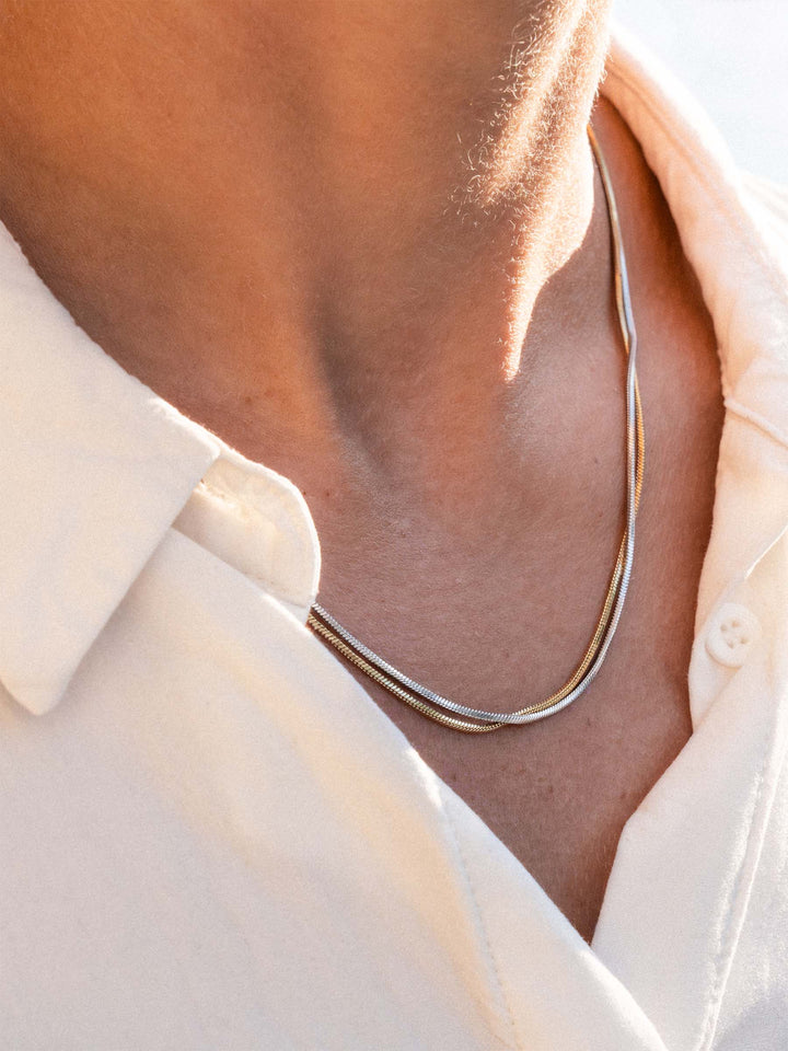 Close-up of a person wearing a silver and a gold necklace with a light-colored shirt.